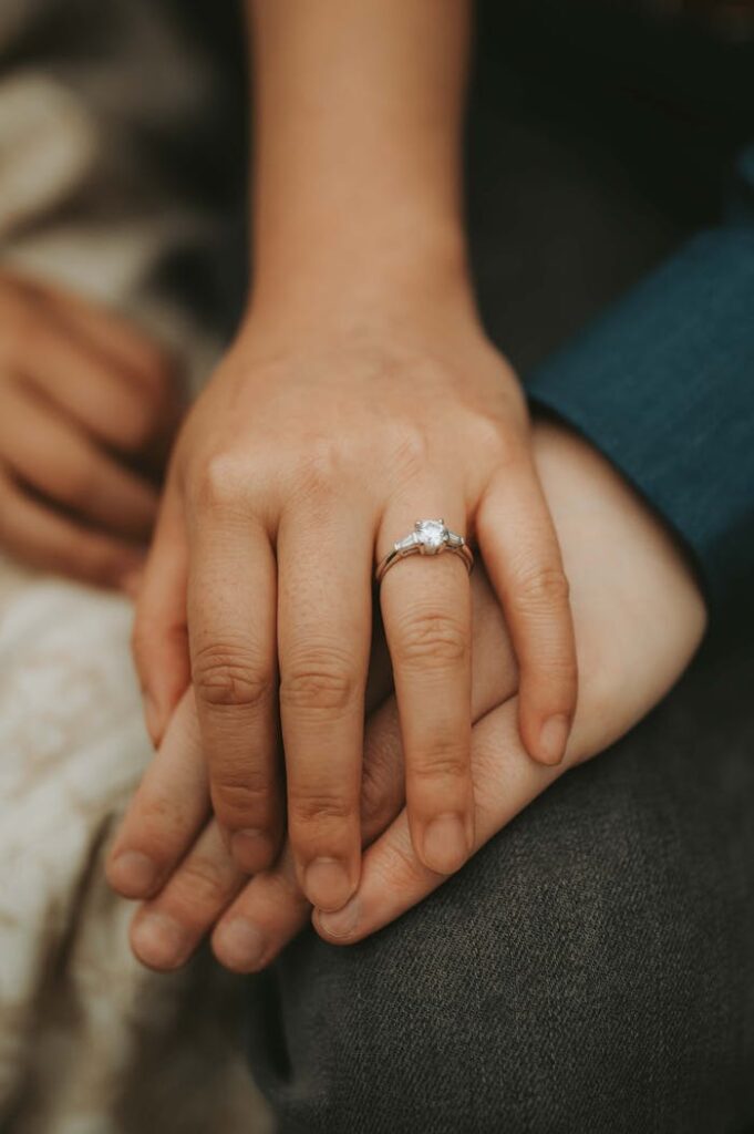 Close-up of a couple holding hands, showcasing an elegant engagement ring, symbolizing love and commitment.