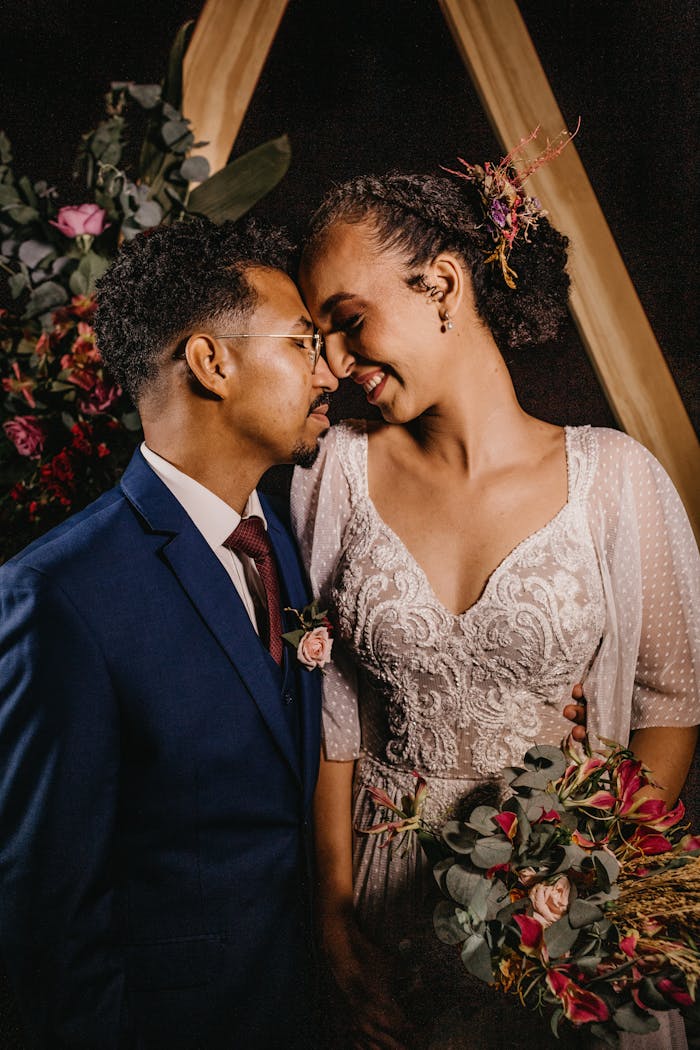 Young dreamy black groom in suit embracing content bride with closed eyes in evening during festive event